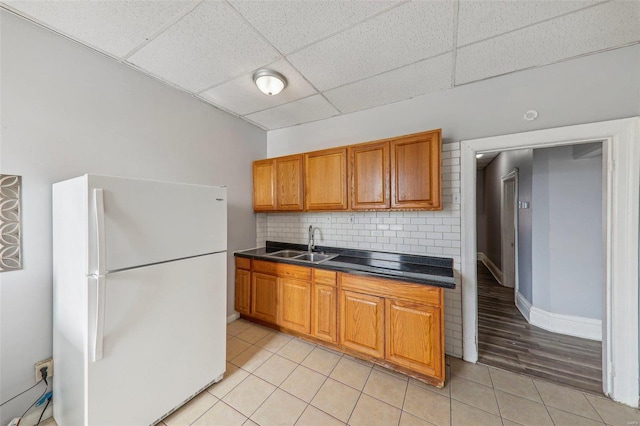 kitchen featuring white refrigerator, sink, a drop ceiling, light tile patterned floors, and tasteful backsplash