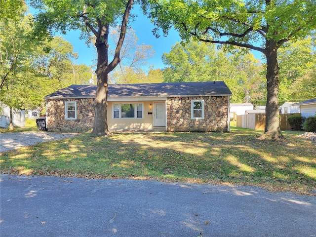 single story home with stone siding, fence, and a front lawn