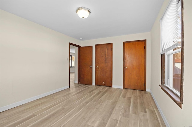 unfurnished bedroom featuring multiple closets, light wood-type flooring, and baseboards