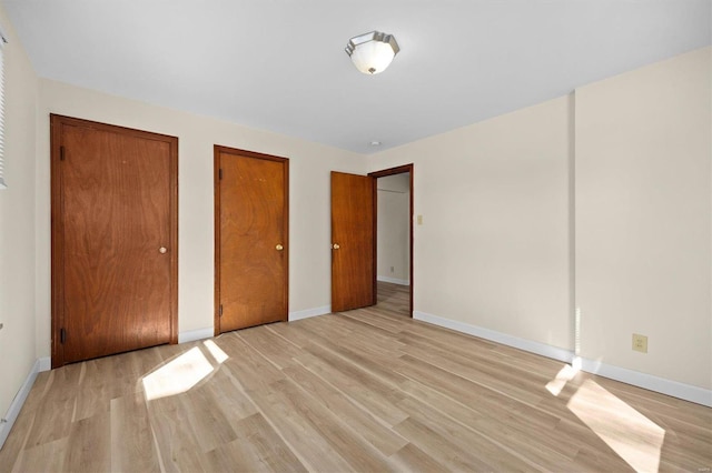 unfurnished bedroom with light wood finished floors, baseboards, and two closets