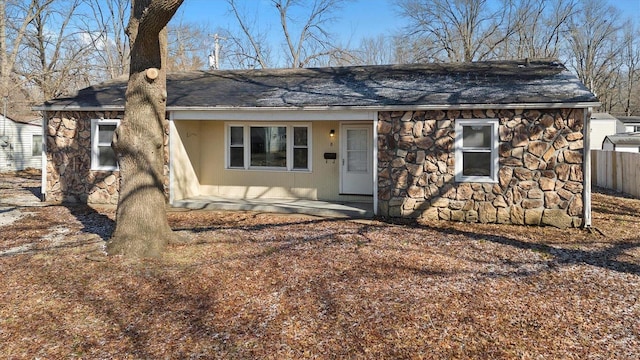 view of front of home with a shingled roof, stone siding, fence, and a patio