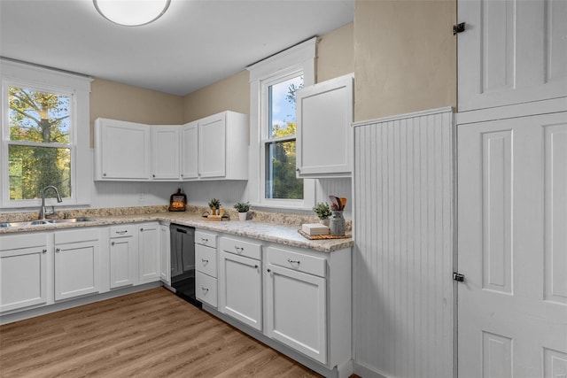 kitchen with black dishwasher, light stone countertops, sink, light wood-type flooring, and white cabinets