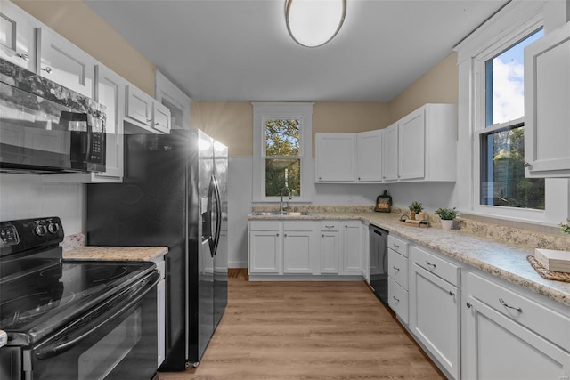 kitchen featuring light hardwood / wood-style floors, white cabinetry, black appliances, and plenty of natural light