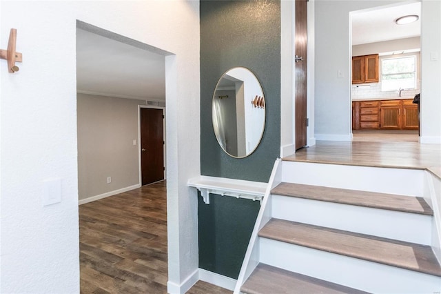 stairway with crown molding, wood-type flooring, and sink