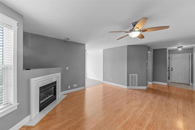 unfurnished living room with ceiling fan, a premium fireplace, and light hardwood / wood-style flooring