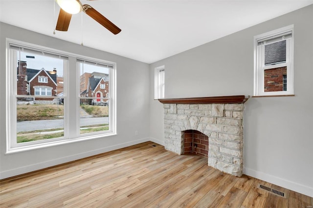 unfurnished living room featuring a wealth of natural light, a fireplace, ceiling fan, and light wood-type flooring