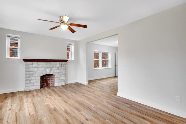 unfurnished living room with light hardwood / wood-style floors, a stone fireplace, ceiling fan, and a healthy amount of sunlight