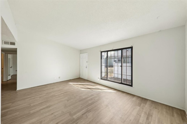 empty room featuring a textured ceiling, wood finished floors, and visible vents