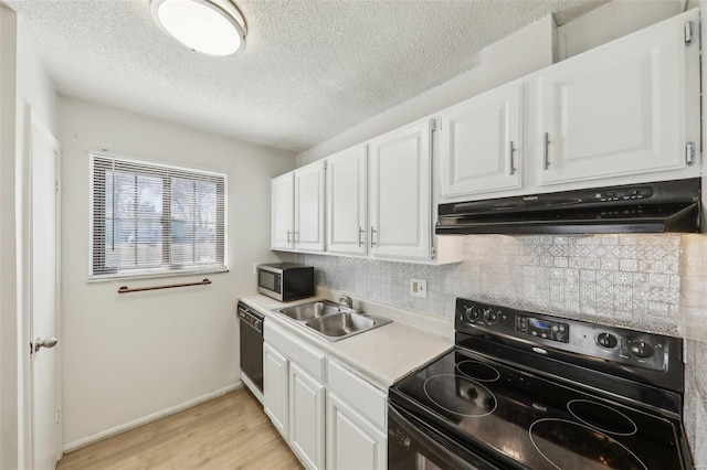 kitchen featuring white cabinetry, a sink, under cabinet range hood, and black appliances