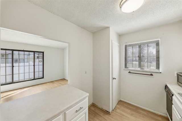 interior space featuring light countertops, light wood-style flooring, white cabinets, a textured ceiling, and baseboards