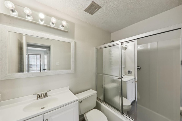 bathroom featuring visible vents, toilet, combined bath / shower with glass door, a textured ceiling, and vanity