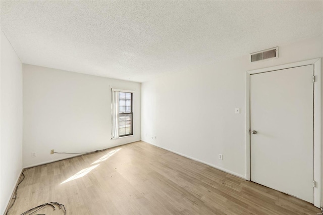 empty room with a textured ceiling, wood finished floors, and visible vents