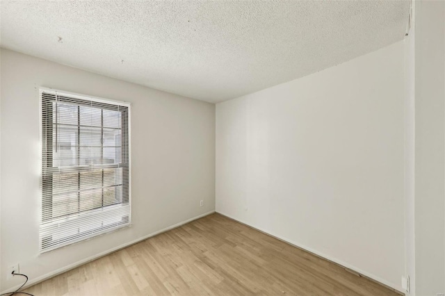 spare room featuring baseboards, light wood-style flooring, and a textured ceiling