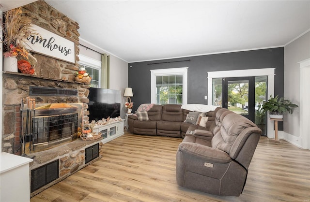 living room with ornamental molding, a stone fireplace, and light hardwood / wood-style floors