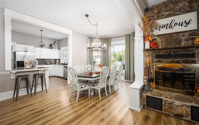 dining room with a fireplace, sink, a notable chandelier, light hardwood / wood-style floors, and crown molding