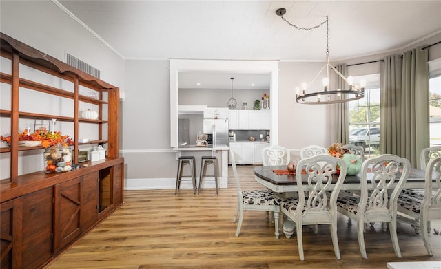 dining space featuring crown molding, light wood-type flooring, and a notable chandelier