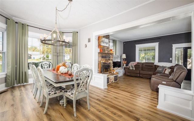 dining area with a notable chandelier, wood-type flooring, ornamental molding, and a fireplace