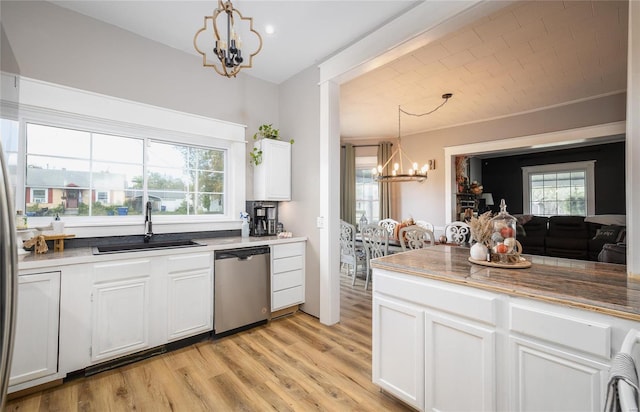 kitchen with sink, white cabinetry, hanging light fixtures, stainless steel dishwasher, and a chandelier