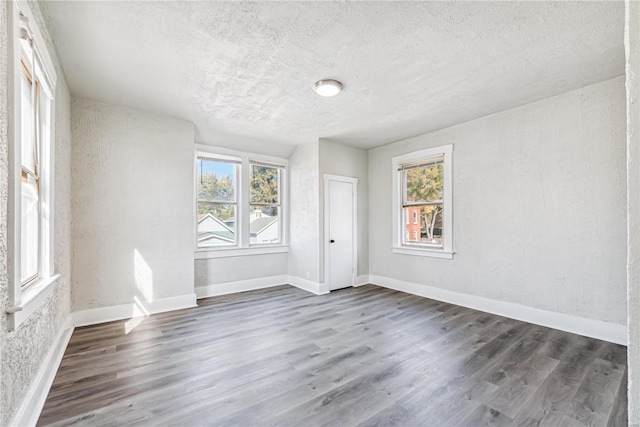 unfurnished room with a textured ceiling, plenty of natural light, and dark hardwood / wood-style floors