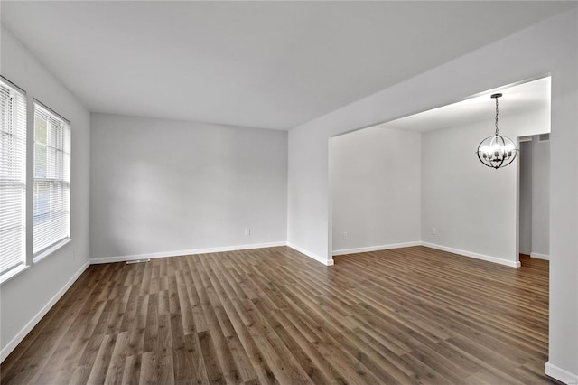 spare room with a notable chandelier and dark hardwood / wood-style flooring