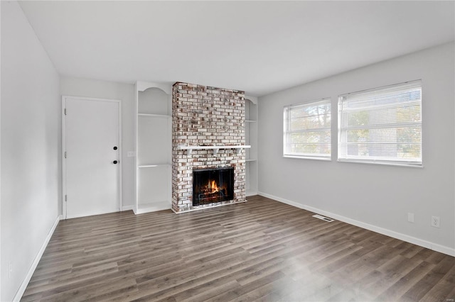 unfurnished living room featuring a brick fireplace and dark hardwood / wood-style floors