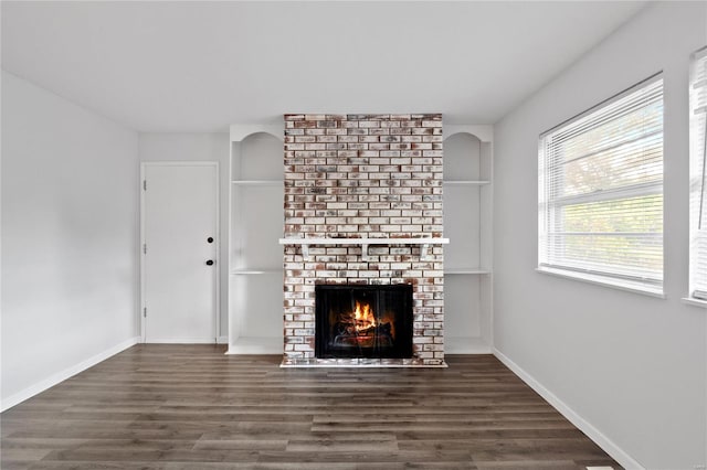 unfurnished living room with dark wood-type flooring and a brick fireplace