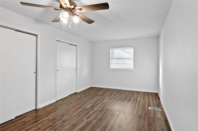 unfurnished bedroom with multiple closets, dark wood-type flooring, and ceiling fan