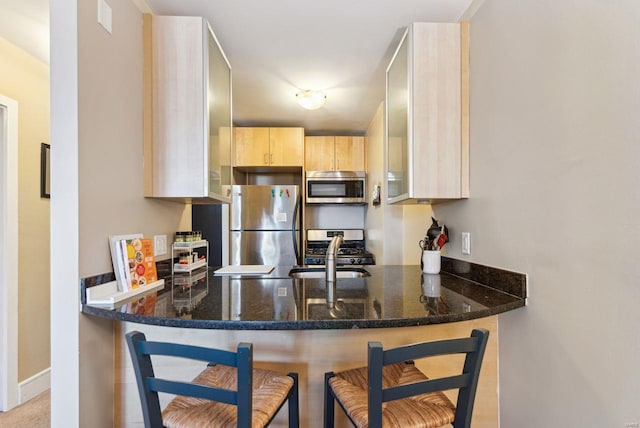 kitchen featuring light brown cabinets, kitchen peninsula, a breakfast bar, and stainless steel appliances