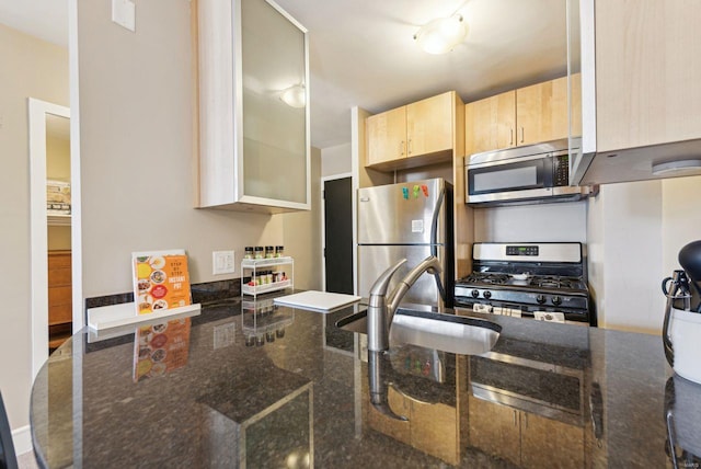 kitchen with stainless steel appliances, dark stone counters, light brown cabinets, and sink