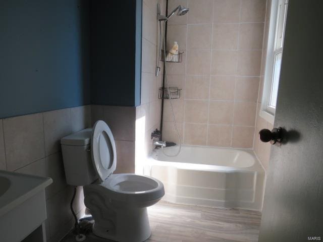 full bathroom with toilet, tiled shower / bath, vanity, and tile walls