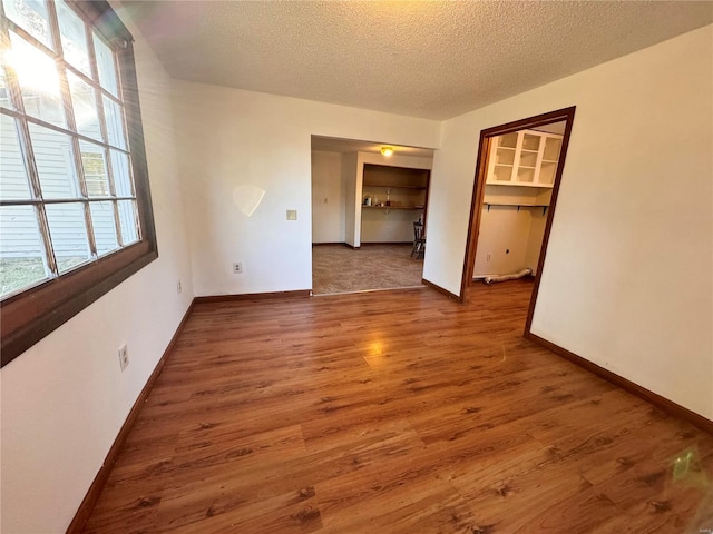 empty room with wood finished floors, a textured ceiling, and baseboards