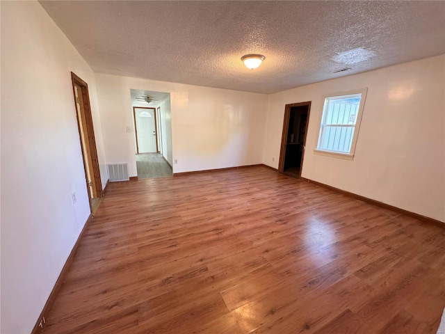 empty room with a textured ceiling, wood finished floors, visible vents, and baseboards