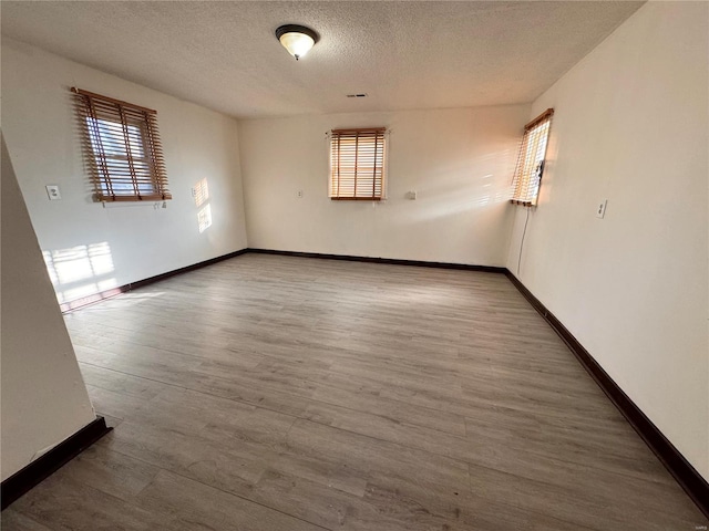 unfurnished room with baseboards, wood finished floors, and a textured ceiling