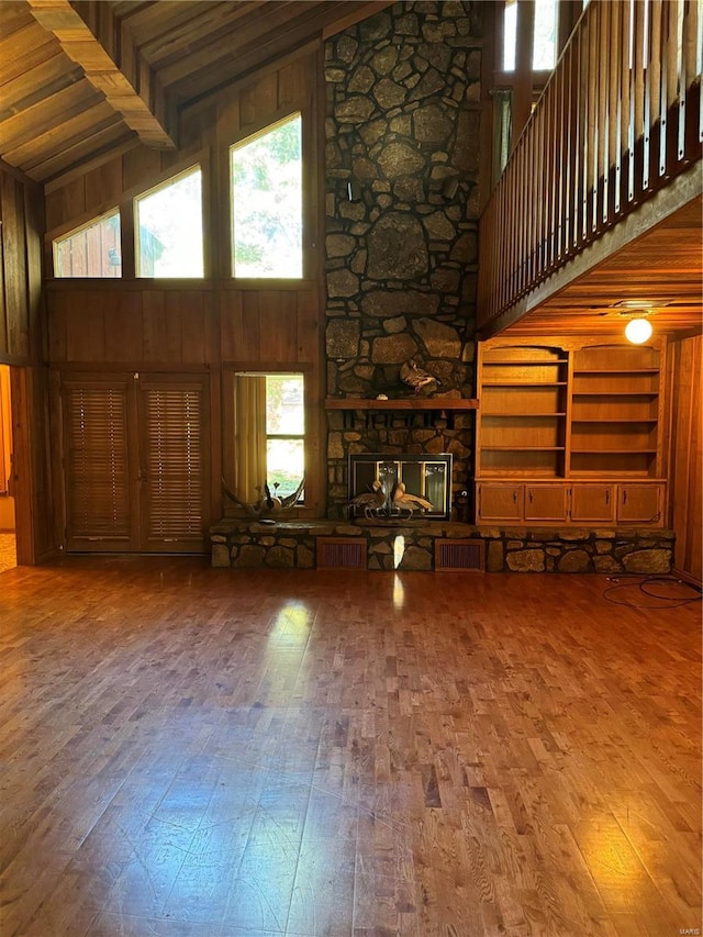 unfurnished living room featuring hardwood / wood-style floors, high vaulted ceiling, wooden ceiling, and wooden walls