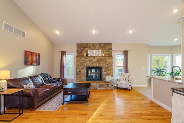 living room featuring sink, lofted ceiling, light wood-type flooring, and a fireplace