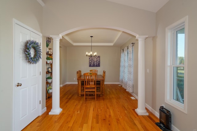 dining space with light hardwood / wood-style floors, a notable chandelier, a tray ceiling, and ornate columns