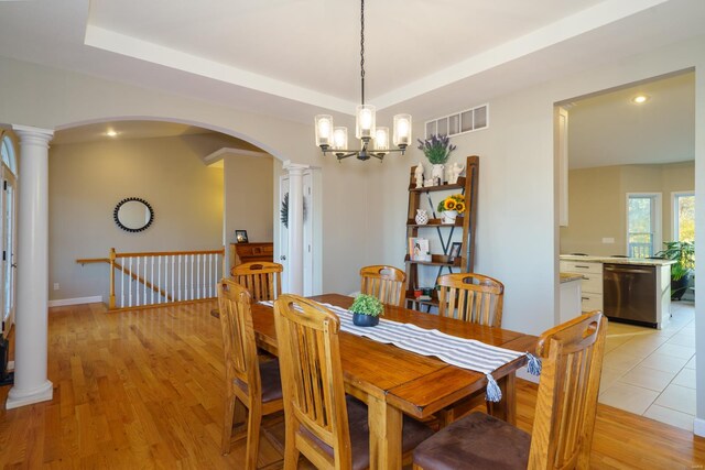 dining room with an inviting chandelier, a tray ceiling, and light wood-type flooring