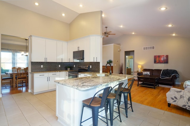 kitchen featuring sink, kitchen peninsula, white cabinetry, stainless steel appliances, and high vaulted ceiling