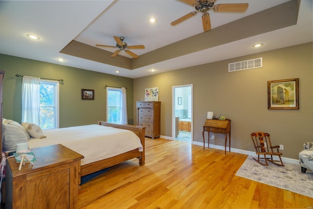 bedroom featuring connected bathroom, ceiling fan, a raised ceiling, and light wood-type flooring