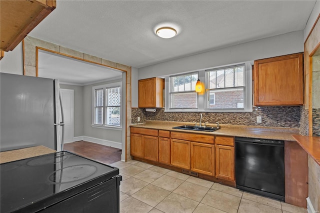 kitchen featuring range with electric stovetop, black dishwasher, stainless steel fridge, sink, and light tile patterned floors