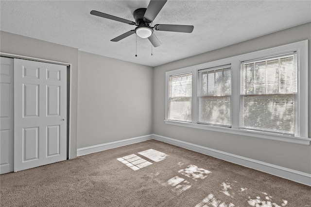 carpeted empty room featuring a textured ceiling, ceiling fan, and a wealth of natural light