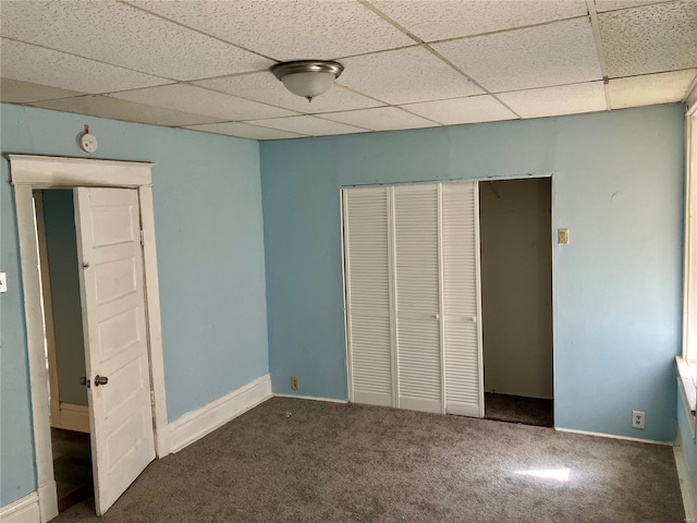 unfurnished bedroom with a closet, a paneled ceiling, and dark colored carpet