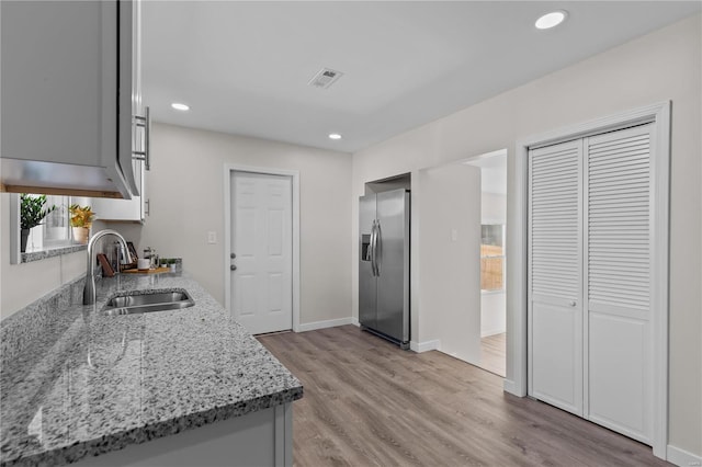 kitchen featuring light stone counters, sink, light hardwood / wood-style flooring, and stainless steel refrigerator with ice dispenser