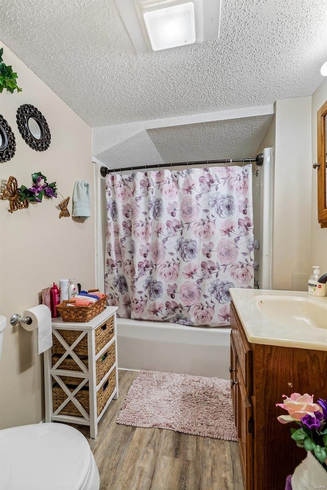 full bathroom with a textured ceiling, hardwood / wood-style flooring, toilet, shower / bath combo, and vanity