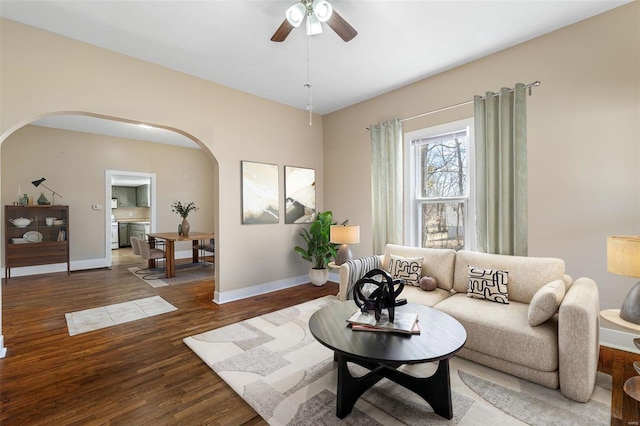 living area featuring arched walkways, wood finished floors, a ceiling fan, and baseboards