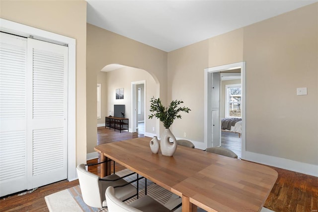 dining space featuring arched walkways, wood finished floors, and baseboards