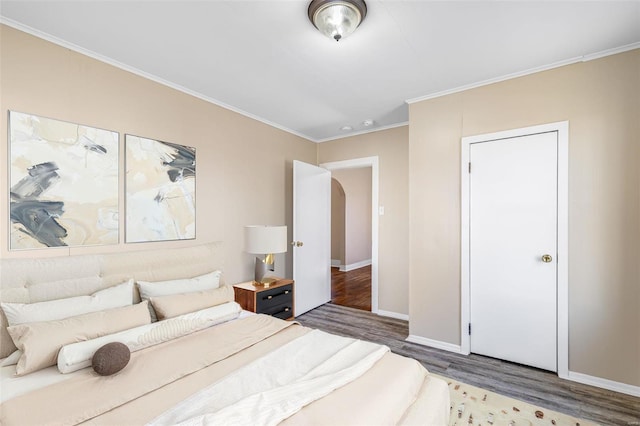 bedroom featuring arched walkways, ornamental molding, wood finished floors, and baseboards