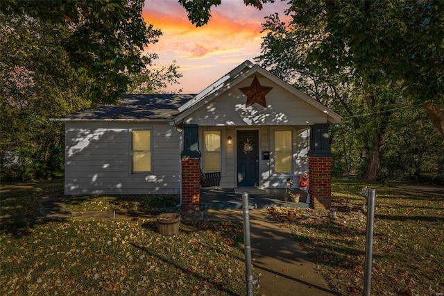 view of front of house with covered porch, brick siding, and a front lawn