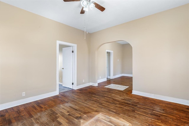 spare room featuring baseboards, arched walkways, ceiling fan, and wood finished floors