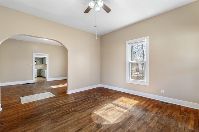 spare room featuring arched walkways, visible vents, baseboards, and wood finished floors